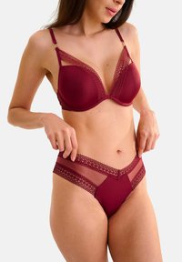 Ensemble de lingerie bordeaux comprenant un soutien-gorge rembourré avec des bordures en dentelle et un slip assorti. Le soutien-gorge présente un design en V profond et des bretelles ajustables.