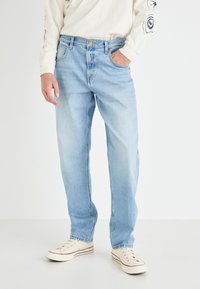 Jeans din denim de un albastru deschis, cu o croială dreaptă, având un design clasic cu cinci buzunare și o ușoară decolorare. Purtați cu adidași de culoare albă-crem.