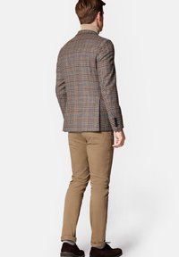 Męska brązowa marynarka w kratę z niebieskimi akcentami i dwoma guzikami, zestawiona z jasnobeżowymi spodniami. Teksturowana tkanina o strukturalnym wzorze.