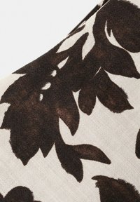 Gros plan sur un tissu beige avec un motif abstrait de feuilles et de branches marron foncé, mettant en valeur la texture tissée et le contraste naturel des couleurs.