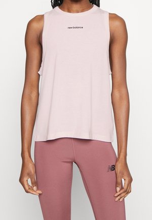 Vrouw draagt lichtroze mouwloze New Balance top en paarse legging met New Balance-logo op dij, staand tegen witte achtergrond.