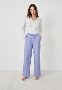 Haut gris à manches longues et pantalon large rayé bleu avec taille élastique et cordon de serrage. Poches des deux côtés, coupe décontractée.