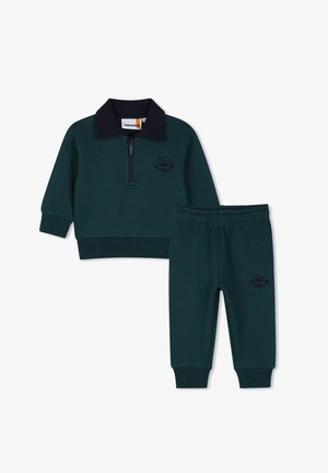 Donkergroene peuteroutfit met lange mouwen ritstop met zwarte kraag en bijpassende broek met elastische taille, beide met Timberland-logo.