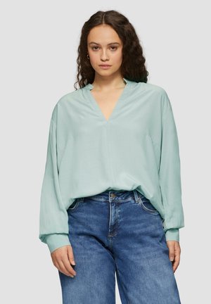 Licht mintgroene blouse met een V-hals en lange, losse mouwen. Zachte, gladde stof valt mooi om de silhouette. Gecombineerd met spijkerbroek.