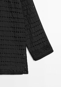 Black semi-sheer blouse sleeve with a grid pattern and floral embroidered cuff detail against a white background.