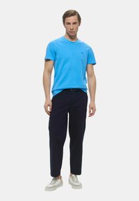 Maglietta di cotone blu con maniche corte abbinata a pantaloni scuri blu navy e sneakers bianche, con un design semplice e colori uniforme.