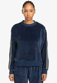 Felpa in velour blu navy con tessuto testurizzato, polsini a costine e una striscia decorativa in tono argento sulle maniche. Scollo semplice a girocollo.