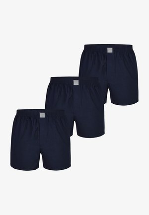 Cajas de algodón en color azul marino con cintura elástica, que presentan una abertura frontal y una etiqueta de tela en la cintura. Se muestran tres pares.