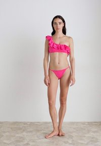 Fuchsiový bikini s jedním ramenem a volánkovým detailem; odpovídající nízké kalhotky. Hladká textura, minimalistický design a živá barva.