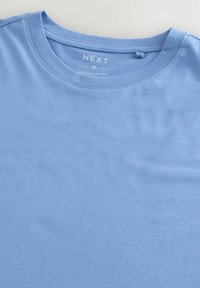 Tricou din bumbac de culoare albastru deschis, cu guler rotund, având un eticheta cu textul "NEXT" și "M REGULAR FIT", cu o textură netedă și mâneci scurte.