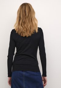 Maglietta nera a maniche lunghe con un silhouette aderente, orlo scallop e tessuto testurizzato, abbinata a una gonna di jeans blu.