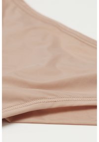 Beige sømløst undertøjsstof med synlige sømme og glat tekstur, foldet på en hvid overflade.