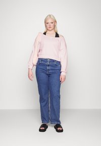 Sweatshirt cropped de ombros à mostra em rosa claro, combinado com jeans de ganga azul de cintura alta e sandálias pretas de slide. Apresenta uma textura suave.