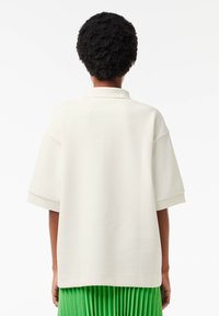 Polo shirt oversize color crema con maniche corte e tessuto testurizzato, caratterizzato da un colletto classico e una vestibilità rilassata, visto da dietro.