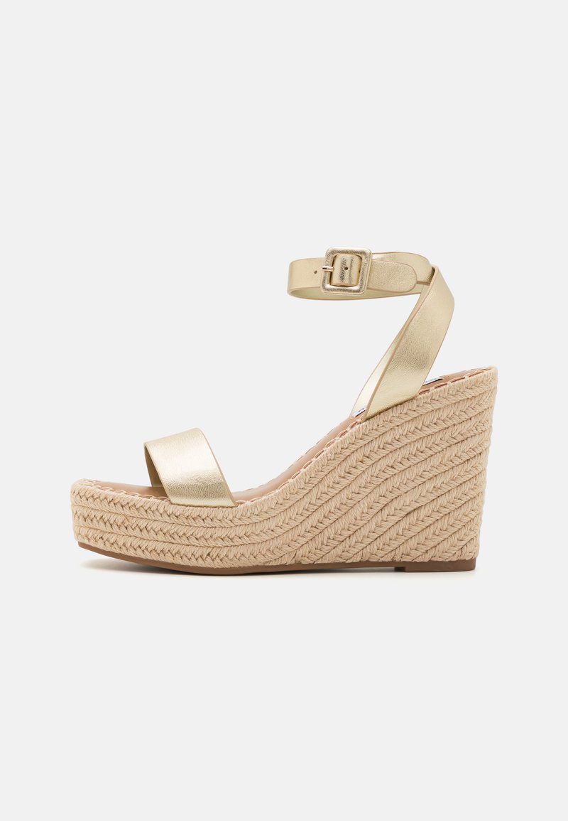 Kaldsadul, millel on kuldmetallist rihm ja pandlaankle rihm. Punutud jute midsole'il on tekstureeritud laineline muster.