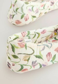 Ballerines en tissu doux avec un motif floral en tons verts, roses et violets, avec une petite étiquette « NEXT » sur le côté.