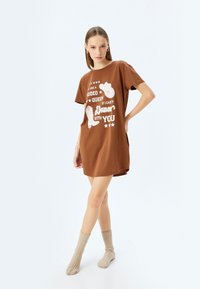 Vestido de camiseta de algodón marrón con un diseño gráfico en blanco con botas de vaquero, ajuste informal, mangas cortas y escote redondo.