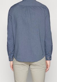 Navyblauw overhemd met lange mouwen, voorzien van een ronde zoom en plooidetail aan de achterkant. Knopen op de manchetten.