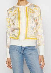 Wzorzysty kardigan z gładkiego materiału, zdobiony pastelowymi motywami kwiatowymi, żółtymi akcentami, okrągłym dekoltem i z przodu na guziki. Żebrowane mankiety i dół.