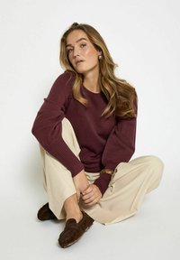 Burgundy knit sweater with ribbed cuffs, paired with cream wide-leg trousers and dark brown loafers, seated on a white background.