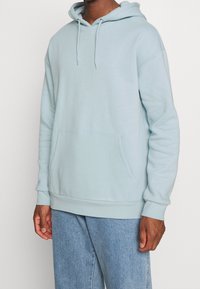 Sudadera con capucha azul claro hecha de tela suave, con bolsillo frontal, capucha con cordón y puños y dobladillo acanalados. Corte relajado.