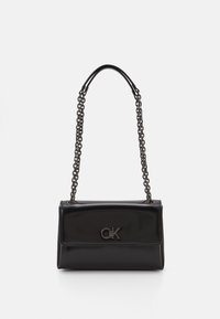 Borsa in pelle nera con una tracolla a catena, con logo CK sul fronte, esposta su uno sfondo bianco.
