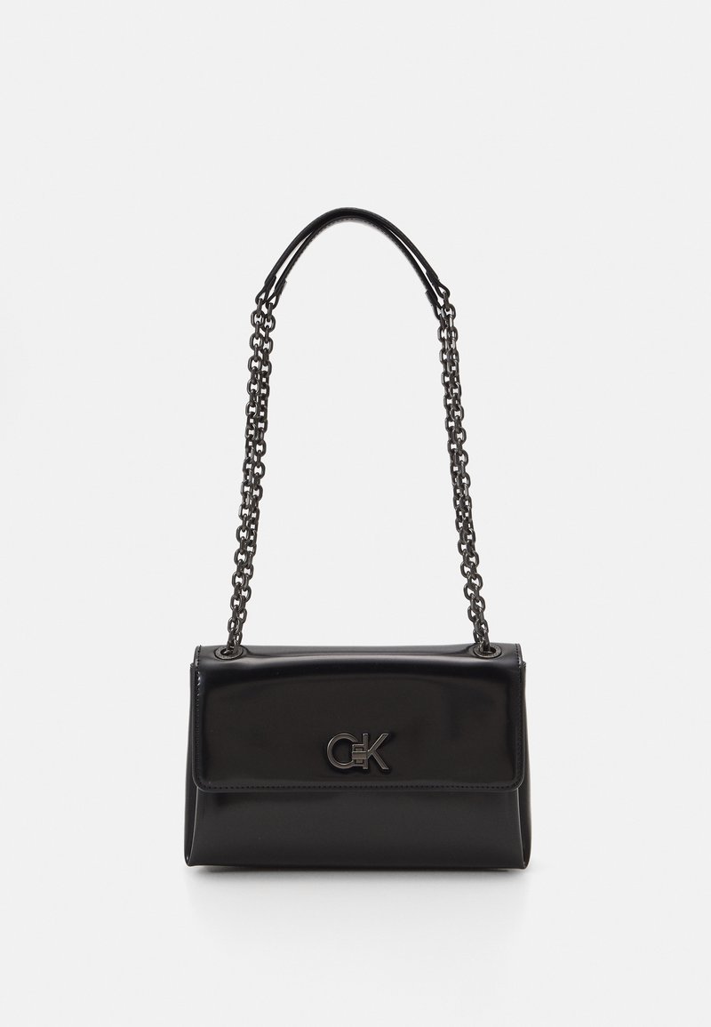 Borsa in pelle nera con una tracolla a catena, con logo CK sul fronte, esposta su uno sfondo bianco.