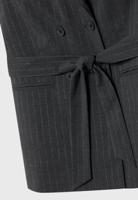 Giacca grigia a righe sottili con design doppiopetto, due bottoni e cintura annodata. Realizzata in un tessuto testurizzato con righe verticali.