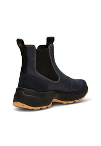 Botas de tobillo azul marino con paneles laterales elásticos, suelas de goma y detalles de costura naranja. Presenta un respaldo texturizado y un talón acolchado.