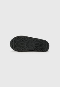 Black rubber shoe sole featuring a geometric tread pattern, rounded toe, and textured surface for traction.