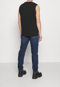 Camiseta sin mangas negra con un corte relajado, acompañada de jeans de denim azul oscuro. Presenta una textura suave y un diseño sencillo. Botas negras a la vista.