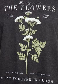 Camisa negra con un estampado floral de flores blancas y hojas verdes. Texto en blanco que dice: "Sé tan libre como las FLORES" y más.