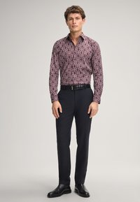 Langärmliges, weinrotes gemustertes Shirt mit taillierter Passform, kombiniert mit dunklen Hosen und schwarzen Stiefeln. Es verfügt über einen klassischen Kragen und eine durchgehende Knopfleiste.