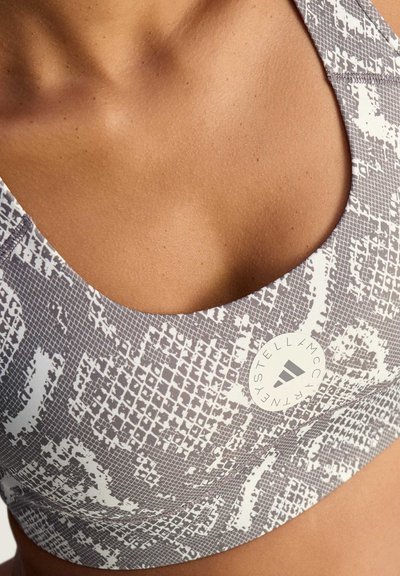 Gray sports bra featuring a textured snakeskin pattern in white, scoop neckline, and a circular logo tag with brand name.