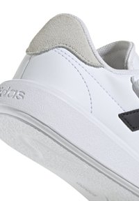 Sneaker bianca con tomaia in pelle liscia, accentuazione in suede grigio sul tallone, logo nero e suola in gomma texturizzata. Presenta un classico design con lacci.