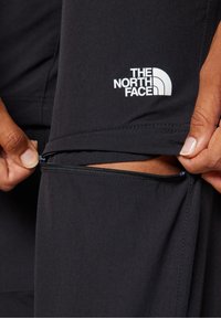 Schwarze Sporthose mit seitlicher Reißverschlusstasche. Verfügt über das weiße The North Face-Logo auf dem linken Oberschenkel, glatte Textur, schlankes Design.