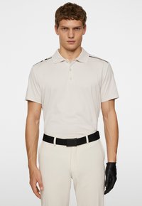 Beige kortärmad polo skjorta med krage, med svarta axelränder. Matchad med ljusa byxor och ett svart bälte.