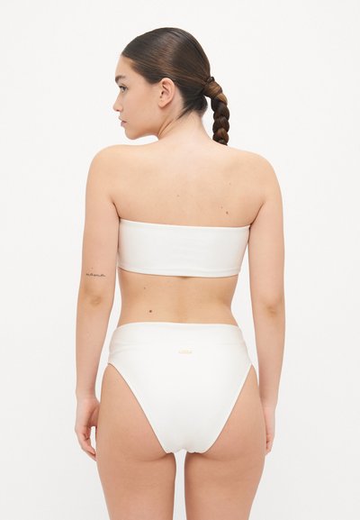 Hvit bandeau bikini topp med høyt liv på bunnene. Glatt stoff, minimal søm, subtilt gulllogo-accent på baksiden.