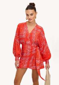 Vestido rojo con patrón de paisley, mangas largas abullonadas, escote en V y un detalle de lazo lateral. Confeccionado en una tela ligera, de textura suave.