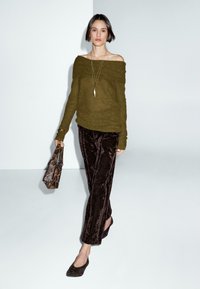 Olivingrüner Off-Shoulder-Pullover, dunkle Samt-Hose und passende schwarze Ballerinas. Die Accessoires umfassen eine goldene Anhänger-Halskette und eine Schlangenprint-Tasche.