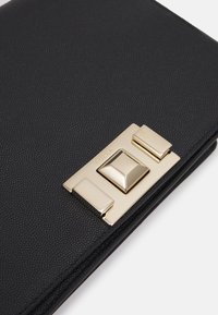 Close-up of a black leather wallet featuring a prominent gold-colored clasp with a pyramid-shaped design, labeled "Furla."