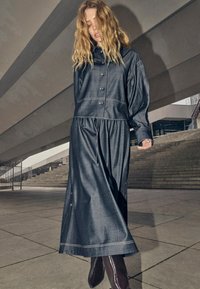 Denim outfit featuring a button-up top with a relaxed fit and a long skirt. Dark blue color with contrasting stitching and side button accents.