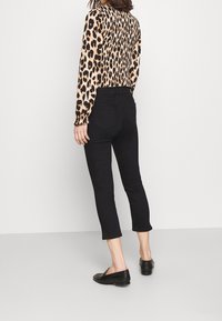 Jeans negros recortados con una cinturilla alta, combinados con una blusa de leopardo de manga larga que presenta mangas fruncidas y un diseño ajustado.