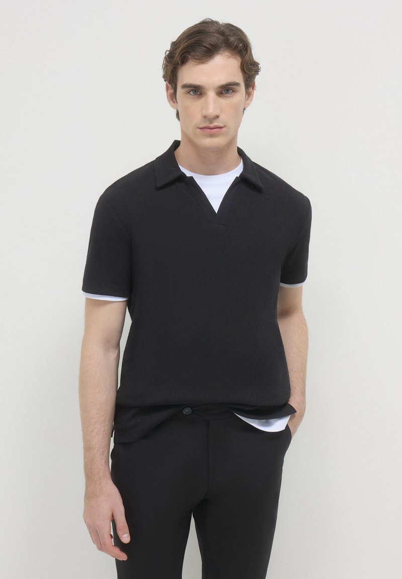 Polo nero a maniche corte con superficie texture, colletto e dettagli bianchi a contrasto sulle maniche. Design slim fit.