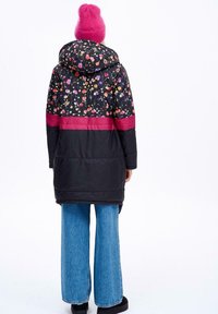 Dlouhá péřová bunda s květinovým vzorem na horní polovině, pevným černým spodem a růžovým pruhem. V kombinaci s širokými džíny a růžovou čepicí.