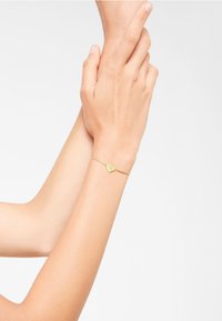 Bracelet en or avec un design délicat de feuilles sur une fine chaîne, illustrant un souci du détail intricate avec une texture lisse et brillante.