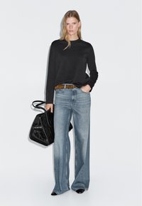 Schwarzes Langarmshirt, hellblaue weite Jeans, brauer Gürtel und eine schwarze strukturierte Handtasche. Abgerundet mit spitzen schwarzen Schuhen.