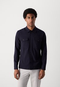 Chemise à manches longues marine avec deux poches poitrine, fermeture à boutons et col. Tissu lisse, coupe droite et poignets à boutons.