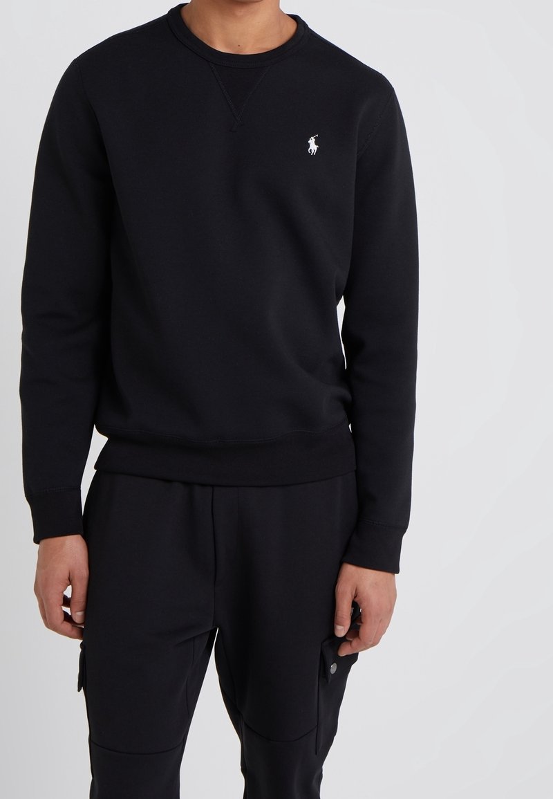 Svart sweatshirt i bomullsblandning med rund halsringning, ribbade ärmslut och midja, prydd med en liten vit logotyp på vänster bröst.