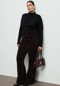 Zwarte nauwsluitende coltrui, donkerbruine uitlopende corduroy broek en een klein bordeauxrood handtasje met gouden beslag. Uitlopende schoenen met textuur.